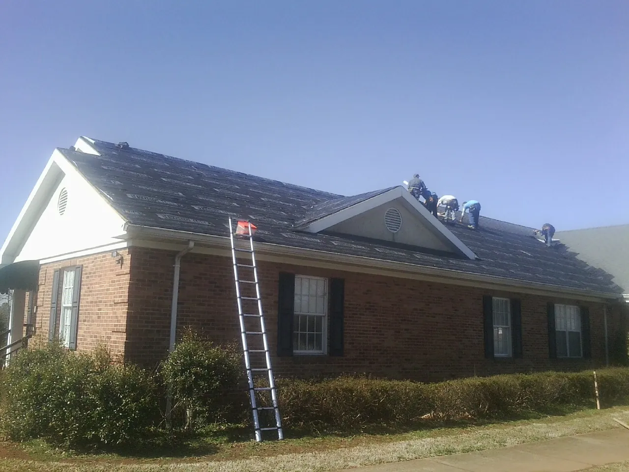 Crew tearing shingles off a brick ranch roof with a ladder set — Emergency Roof Repair work by our crew in North Canton