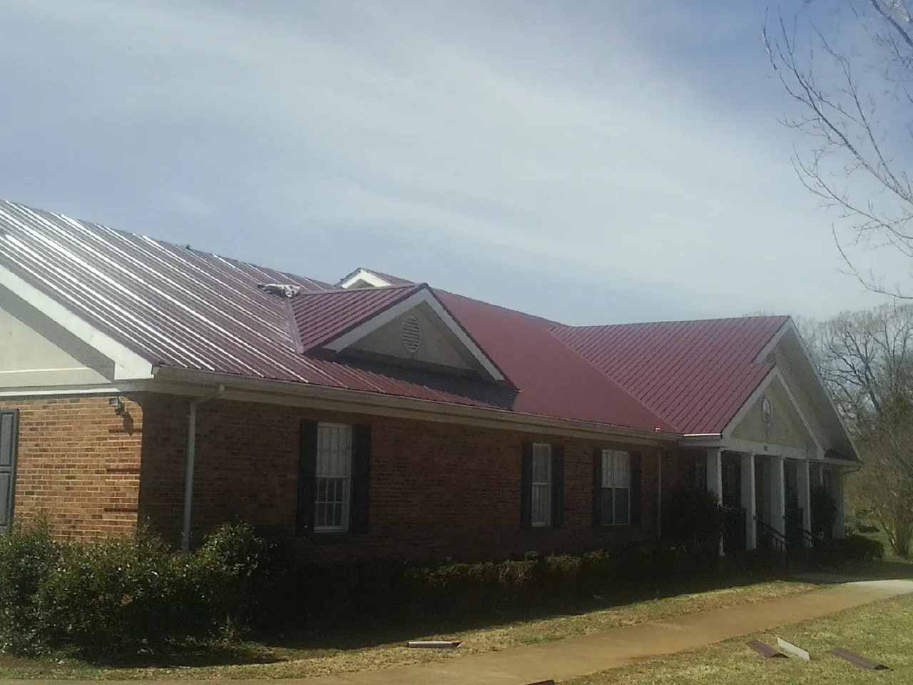 Red metal roof with gabled entries on a long brick building, from a Hail Damage Roof Repair job in North Canton