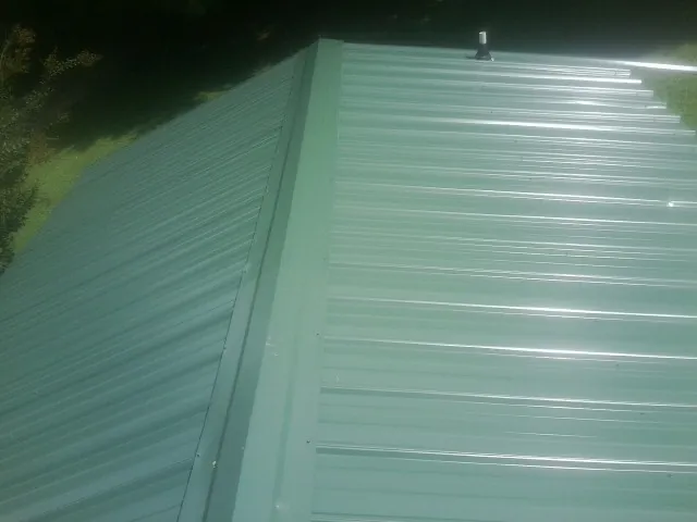 New green metal panels meeting at the ridge of a roof — Flat Roof Repair work by our crew in North Canton