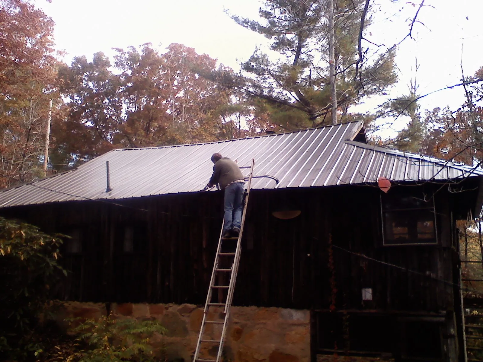 Roofer on a ladder working along the edge of a cabin metal roof in North Canton